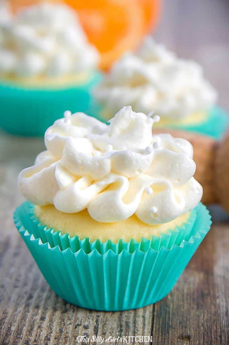A mimosa cupcake in a teal wrapper topped with a tall swirl of champagne buttercream.