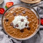 Square image of Chocolate Rice Pudding in clear bowl with whipped cream and chocolate chips.
