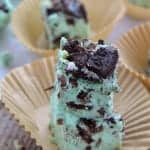 A tall stack of green mint fudge squares loaded with crushed Oreos and Andes mints on a cupcake liner.