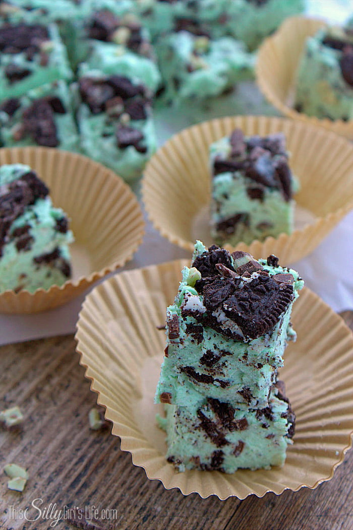Mint Fudge on paper liners stacked with fudge pieces in background.