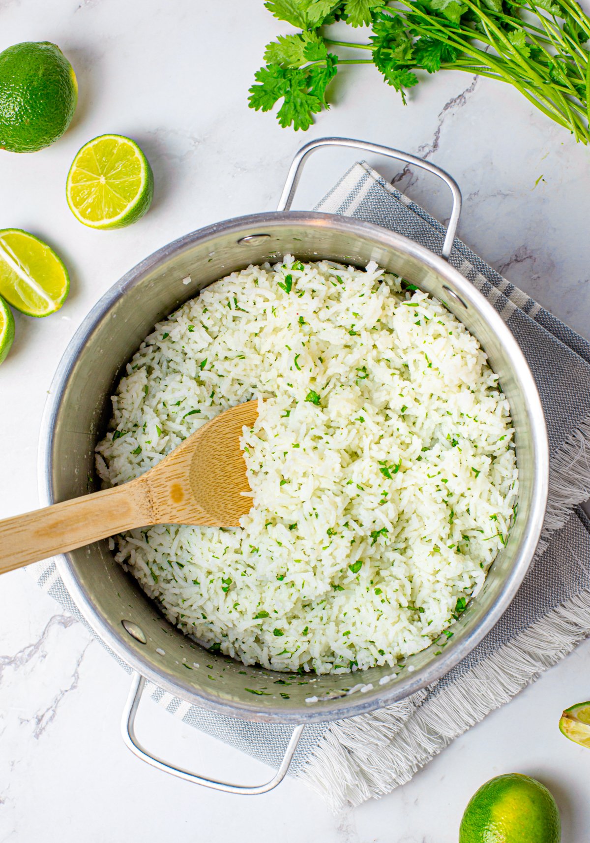 Finished rice in pan with wooden spoon surrounded by limes and cilantro