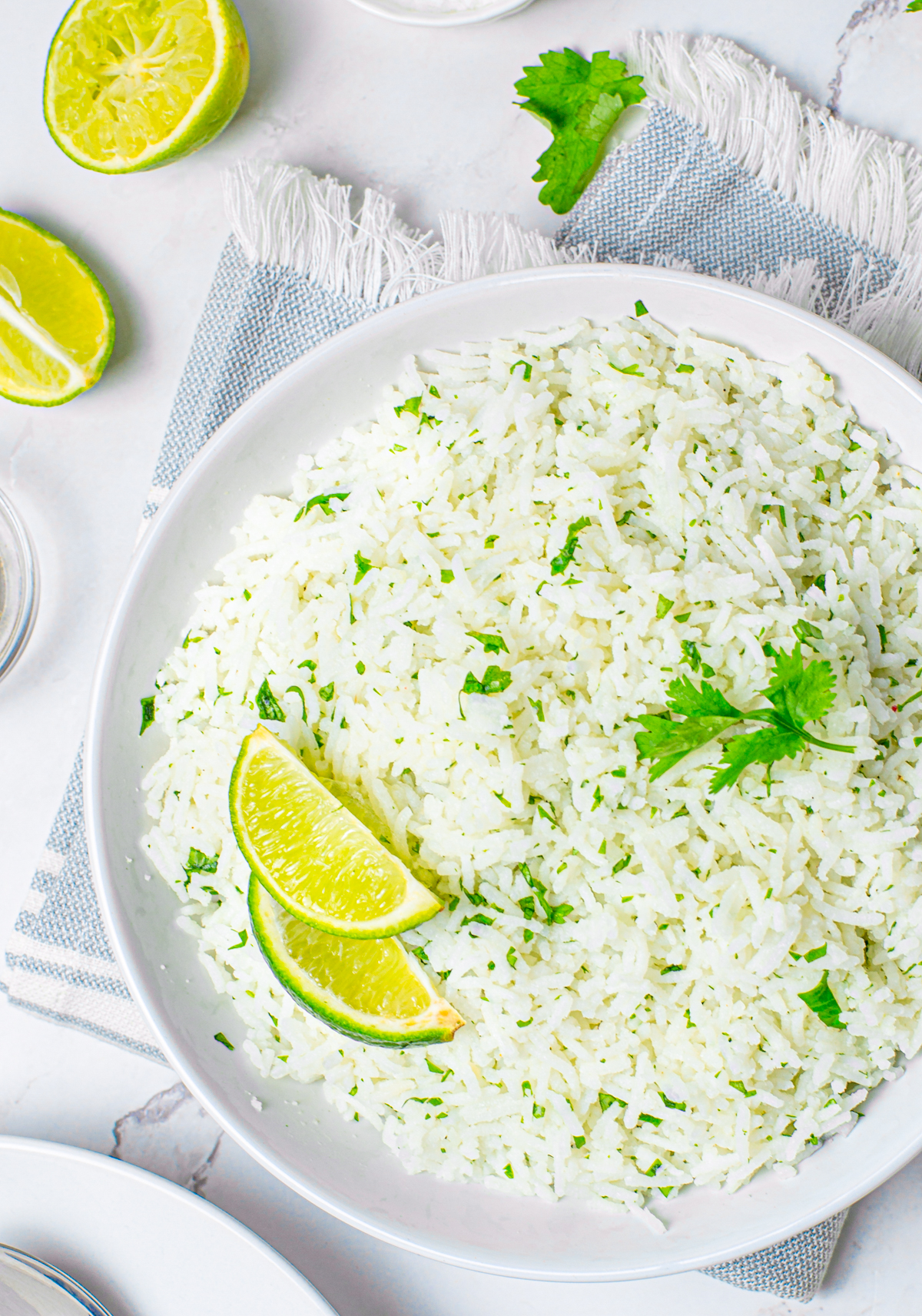 Overhead of rice in white bowl with lime wedges and cilantro