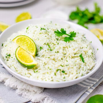 A white bowl of fluffy cilantro lime rice topped with a lime wedge and fresh cilantro