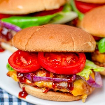 Monterey chicken sliders stacked on a plate with BBQ chicken, bacon, melted cheese, and grilled onions.