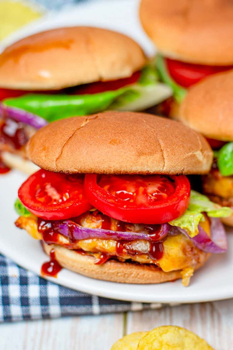 Monterey chicken sliders stacked on a plate with BBQ chicken, bacon, melted cheese, and grilled onions.