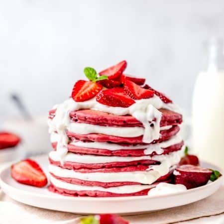 Stacked Red Velvet Pancakes filled with cream cheese fluff and topped with strawberries.