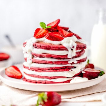 A tall stack of red velvet pancakes layered with cream cheese fluff and topped with fresh strawberries.