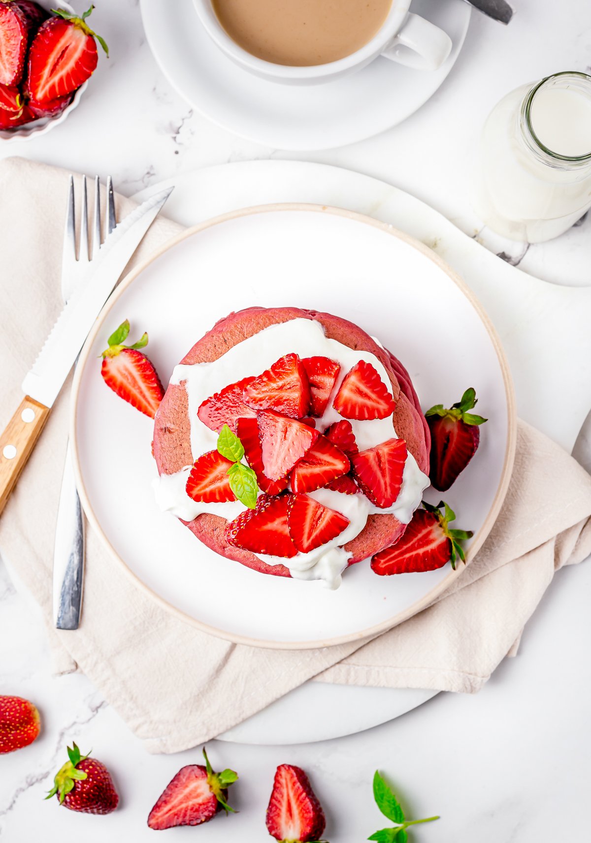 Overhead photo of pancakes stacked on white plate topped with strawberries.