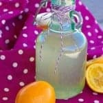 A bottle of homemade lemon simple syrup with a sliced Meyer lemon.
