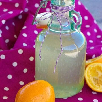 A bottle of homemade lemon simple syrup with a sliced Meyer lemon.
