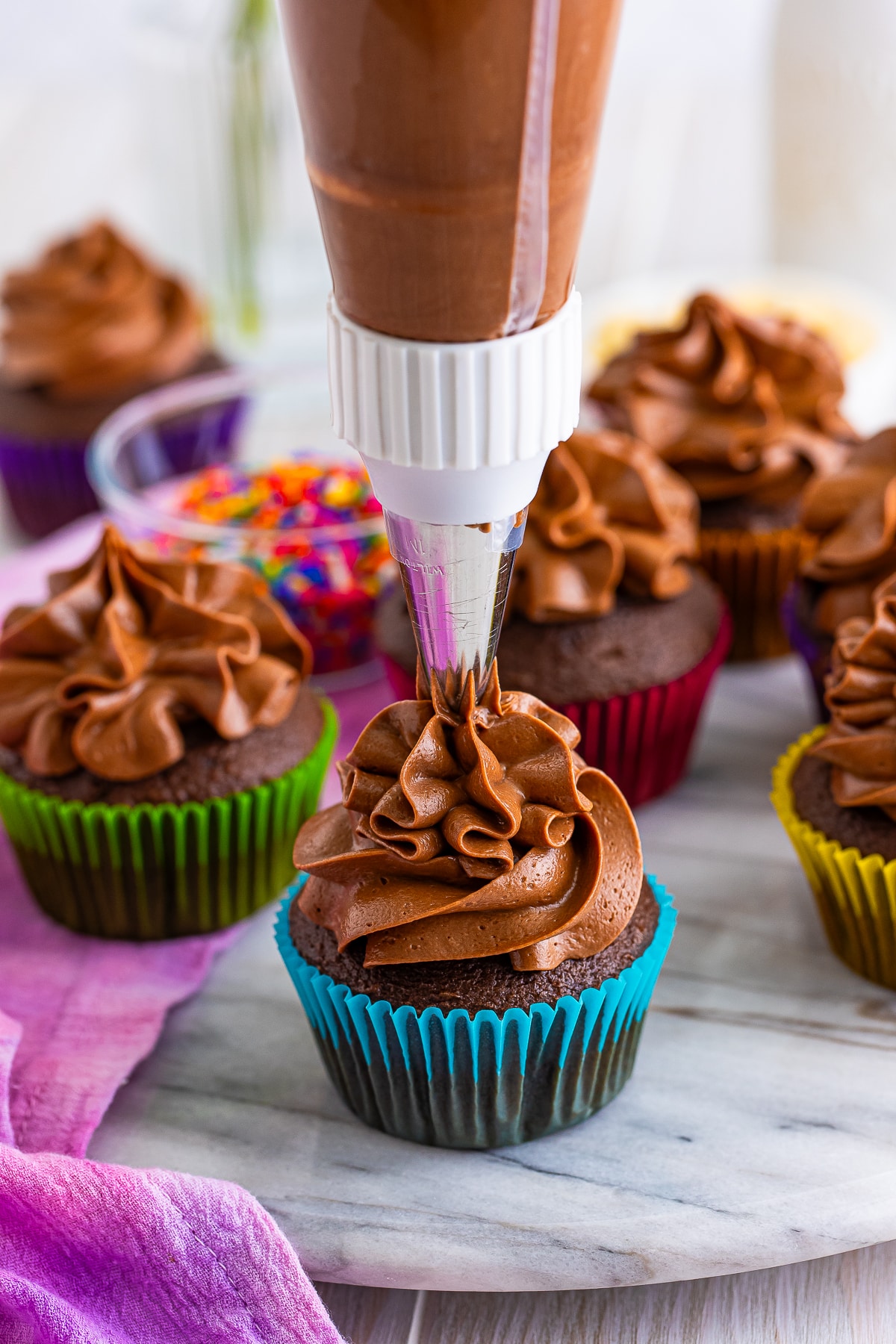a pastry bag piping Chocolate Buttercream Frosting onto a cupcake