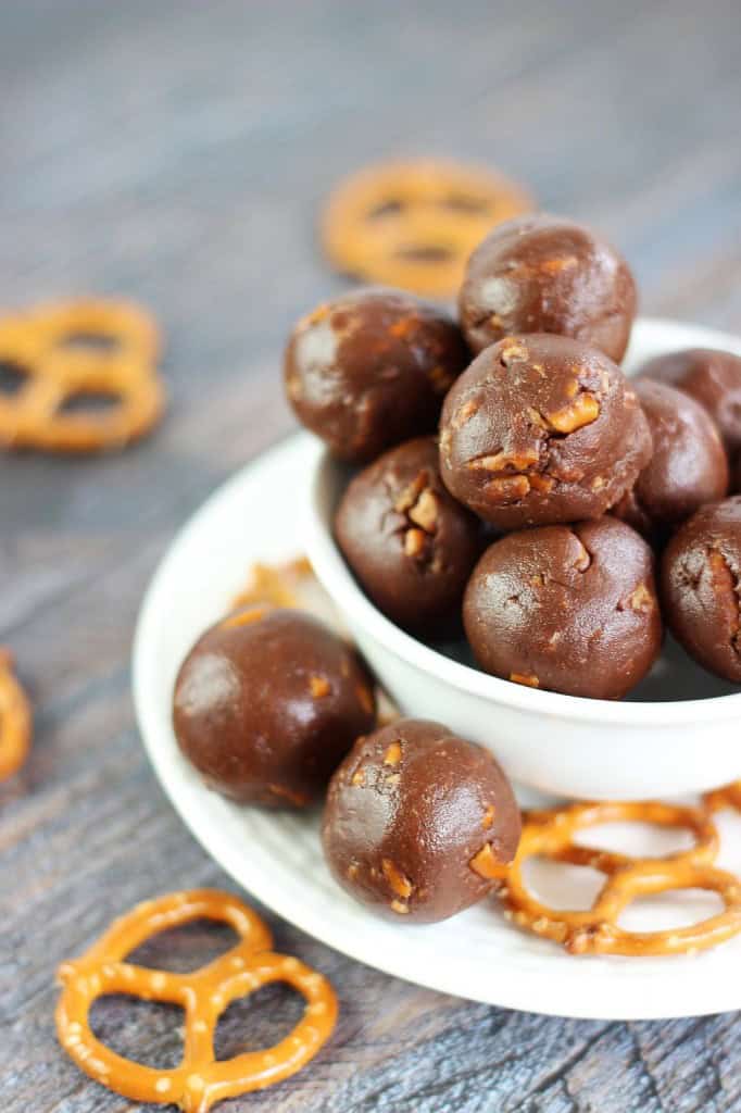 Nutella truffles in a white bowl on a plate scattered with mini pretzel twists.