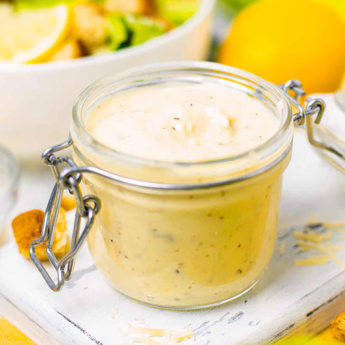 A jar of homemade Caesar salad dressing with lemon and croutons beside it.