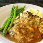 Mushroom Gravy poured over grilled chicken with mashed potatoes and asparagus on a white plate.
