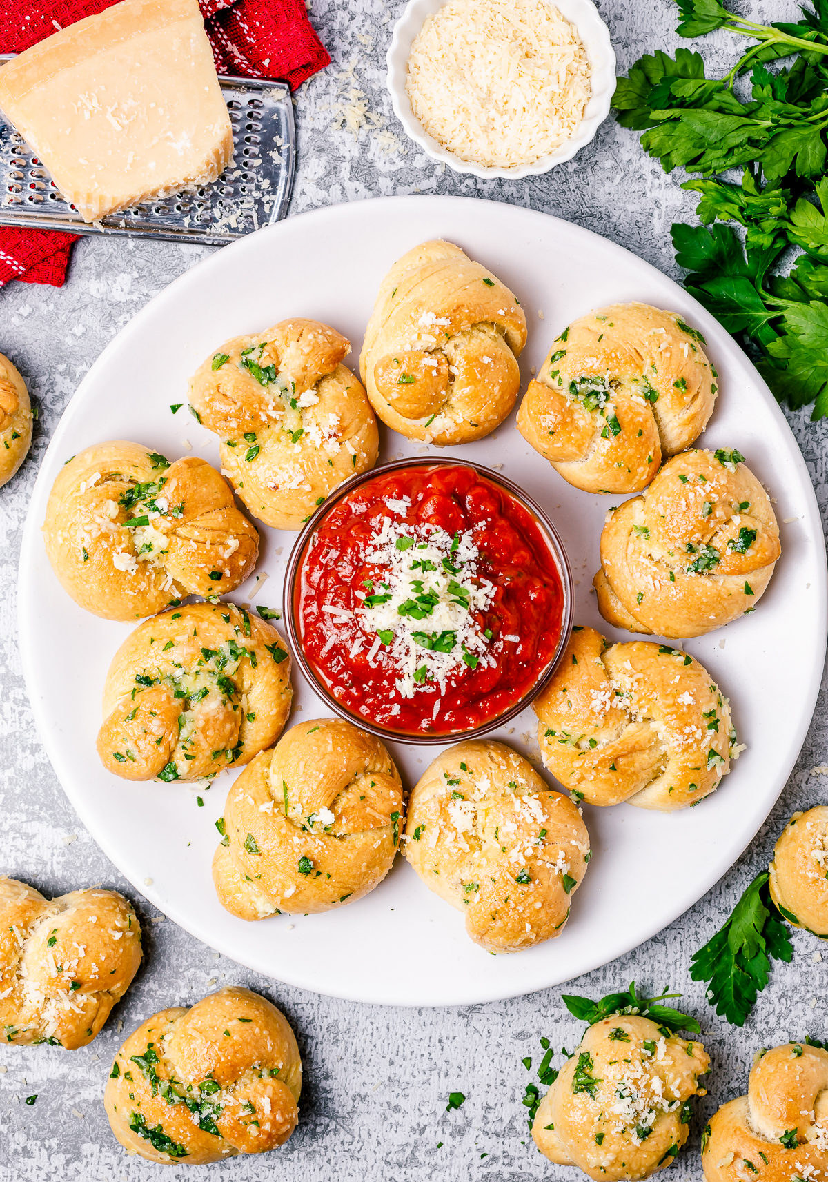 Overhead photos of Garlic Knots Recipe on white plate with marinara sauce in center.