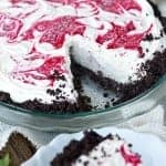 A whole no bake white chocolate raspberry cheesecake with a raspberry swirl on top in an Oreo crust.