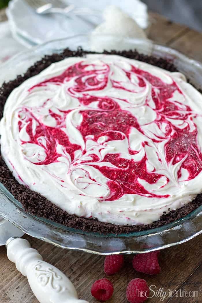 Top down view of a no bake white chocolate raspberry cheesecake with a red raspberry swirl.