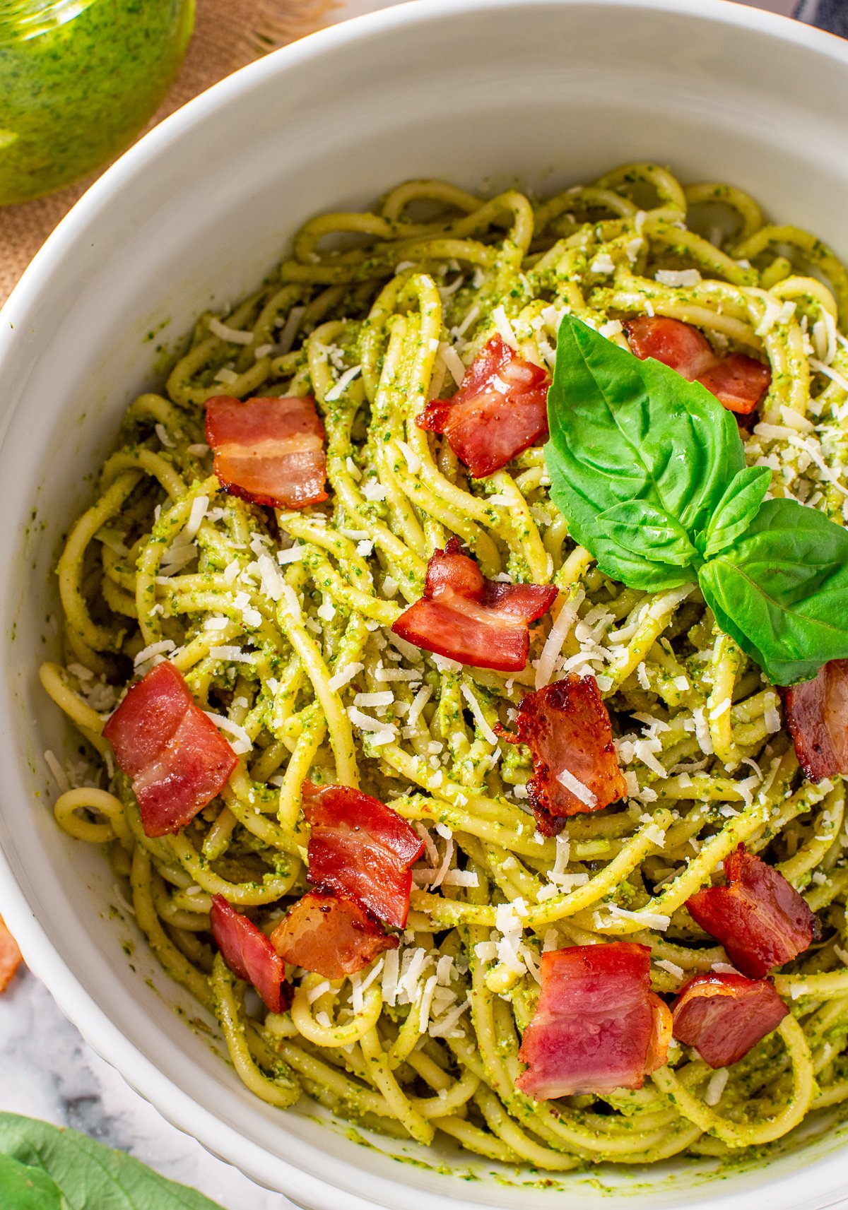 Close up overhead of Bacon Pesto Pasta topped with bacon pieces and basil.
