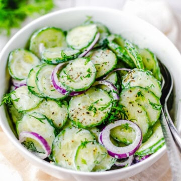 Close up square image of salad in white bowl with two spoons