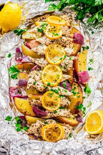 A baked Italian lemon chicken foil packet with browned chicken, potatoes, red onion, and lemon slices.