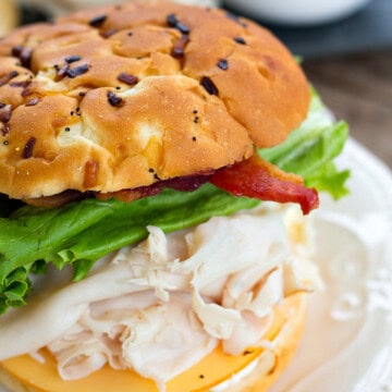 An ultimate turkey bacon cranberry sandwich on a toasted onion roll on a white plate.