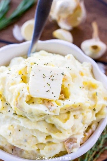 A bowl of creamy roasted garlic mashed potatoes topped with butter and fresh herbs.
