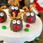 Christmas Oreo balls decorated as Rudolph reindeer with pretzel antlers and red candy noses on a cake stand.
