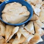 A blue bowl of creamy cookie butter dip surrounded by cinnamon sugar tortilla chips.