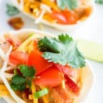 Two slow cooker crack chicken tacos in soft tortillas loaded with creamy shredded chicken, crispy bacon, diced tomatoes, and fresh cilantro.