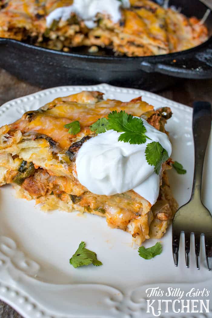 A plated slice of cheesy Mexican lasagna with a dollop of sour cream and cilantro.
