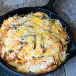 A cast iron skillet of Mexican lasagna topped with melted cheese and sour cream.