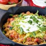 Totchos in a cast iron skillet layered with refried beans, cheese, guacamole, sour cream, and cilantro.