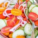 A bowl of cucumber salad with tomatoes and red onion in a sweet vinegar dressing