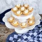 Sugar cookie cups filled with pumpkin cream and whipped cream arranged on a two tier white cake stand.