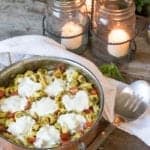 A copper pan of Tortellini Bake with melted mozzarella rounds and blistered grape tomatoes.