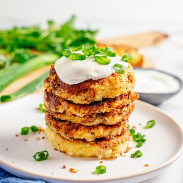 A stack of loaded mashed potato cakes topped with sour cream and scallions.