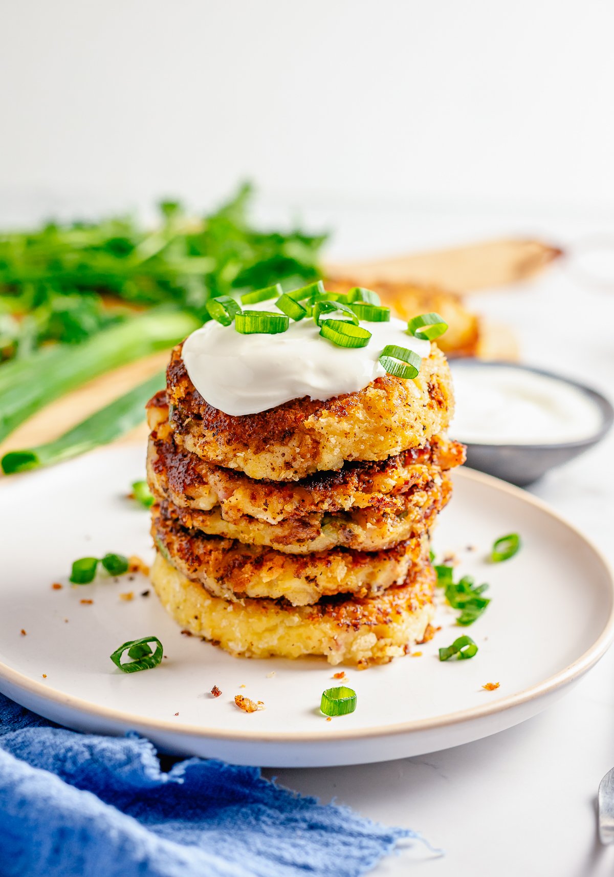 Stacked Loaded Mashed Potato Cakes on white plate with sour cream and scallions.