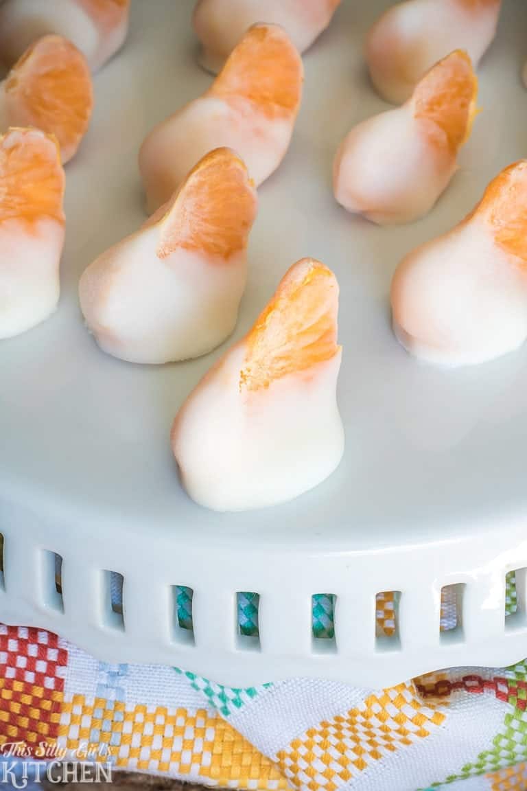 Frozen Yogurt Bites lined up on a white cake stand with clementine segments peeking from the yogurt.