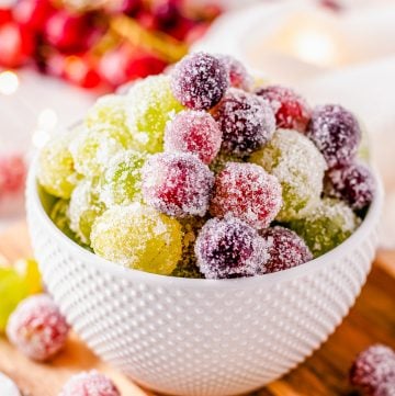 Candied Grapes in a small white bowl with sparkly sugar coating on a wooden cutting board.