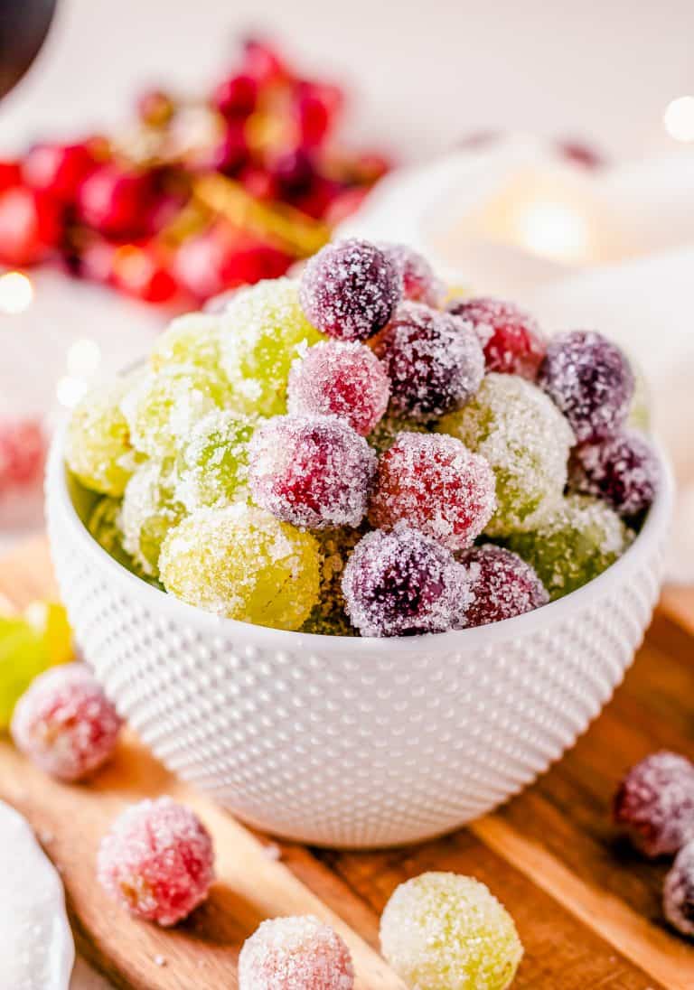 Candied Grapes in a small white bowl with sparkly sugar coating on a wooden cutting board.