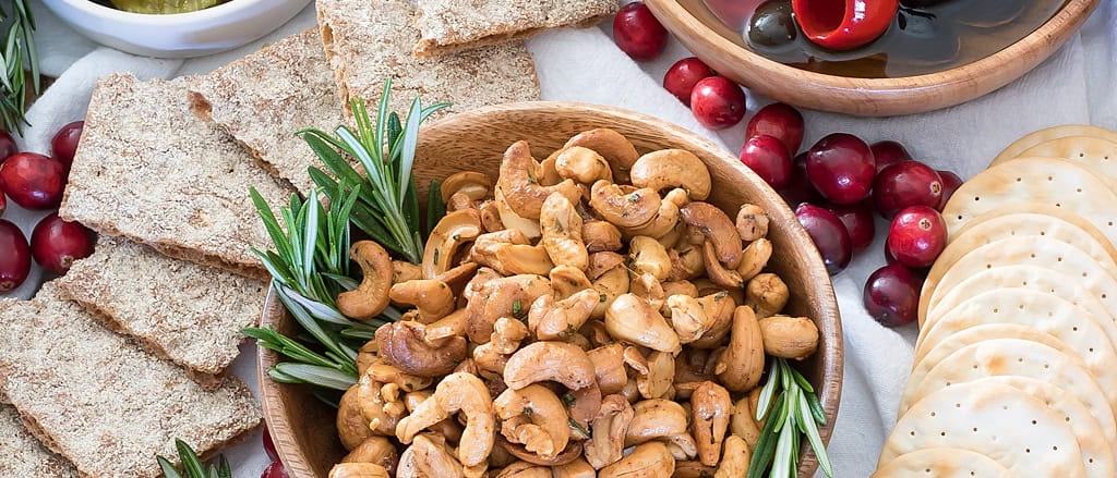 Warm roasted cashews tossed with rosemary butter piled in a wooden serving bowl with crackers alongside.