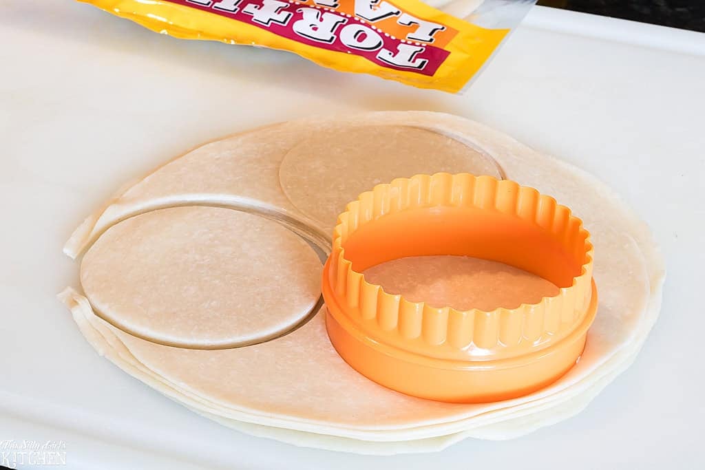 Flour tortillas being cut into rounds with an orange cookie cutter.