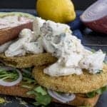 Fried green tomato sandwich stacked with crab salad, arugula, and red onion on toasted white bread.