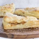 Apple turnovers dusted with powdered sugar on a wooden board.