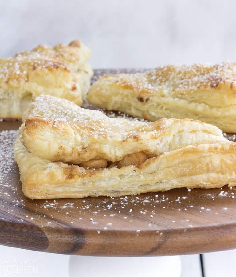 Apple turnovers dusted with powdered sugar on a wooden board.