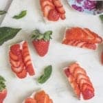 Strawberry tea sandwiches topped with fanned fresh strawberries on a marble board.