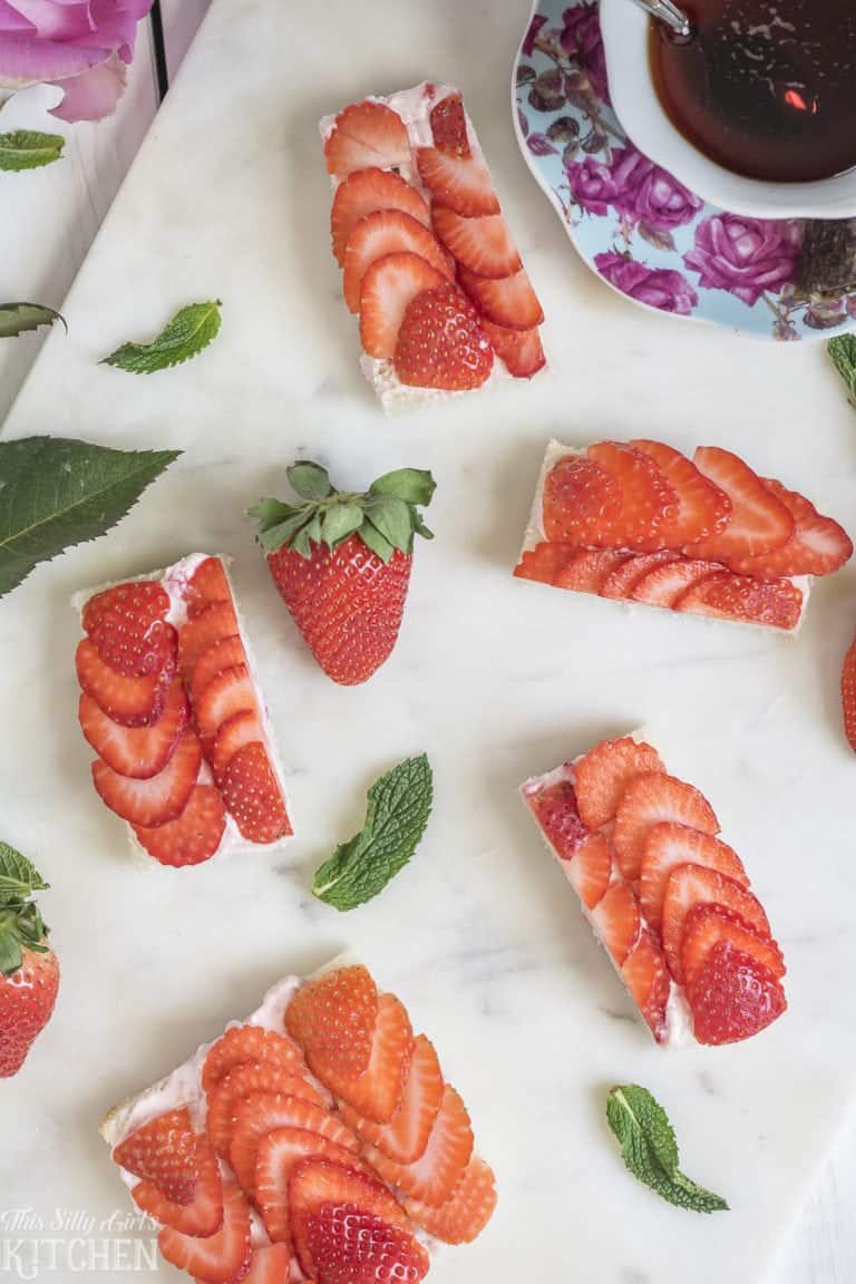 Strawberry tea sandwiches topped with fanned fresh strawberries on a marble board.