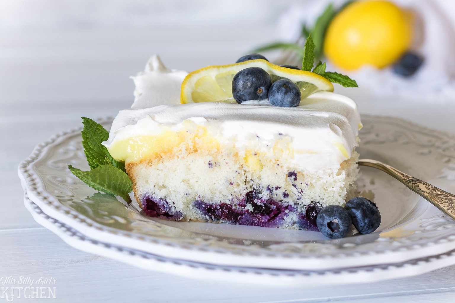 Lemon Blueberry Poke Cake, white cake loaded with fresh blueberries, lemon pudding and whipped topping! Recipe from ThisSillyGirlsKitchen.com