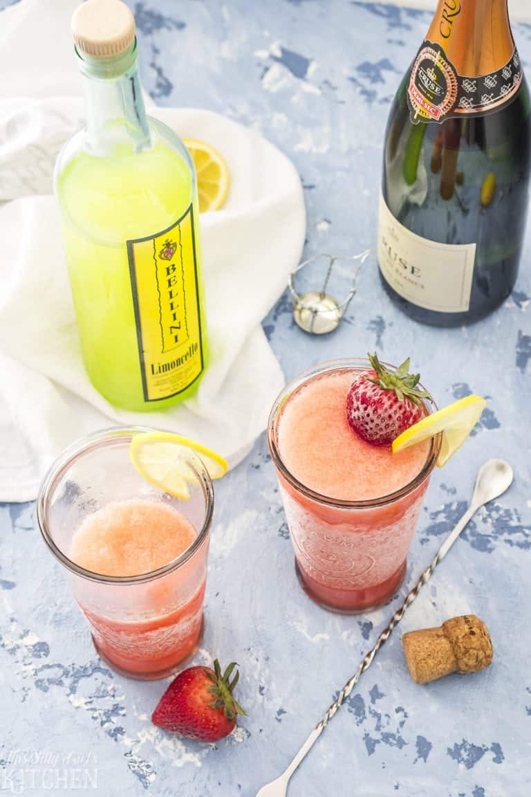 Two glasses of strawberry limoncello slush with a limoncello bottle and sparkling wine.