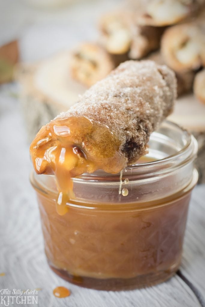 One Roll Up dripping with caramel sauce on top of glass jar of sauce.